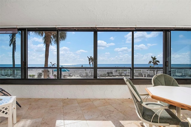 sunroom with plenty of natural light, a beach view, and a water view