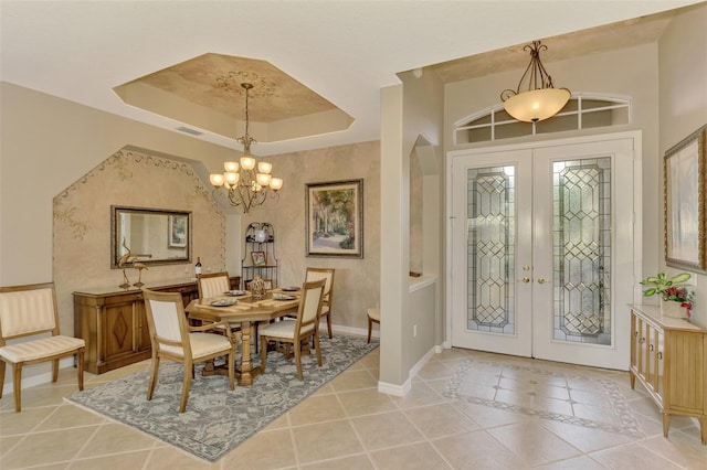 tiled entrance foyer with a tray ceiling, a notable chandelier, and french doors