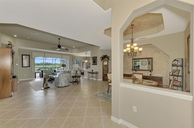 tiled living room featuring a raised ceiling and ceiling fan with notable chandelier