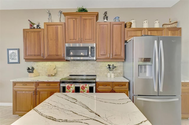 kitchen with light tile patterned floors, light stone countertops, appliances with stainless steel finishes, and tasteful backsplash