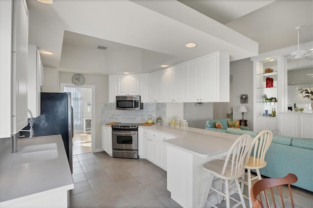 kitchen featuring white cabinets, appliances with stainless steel finishes, a kitchen breakfast bar, kitchen peninsula, and light tile patterned floors