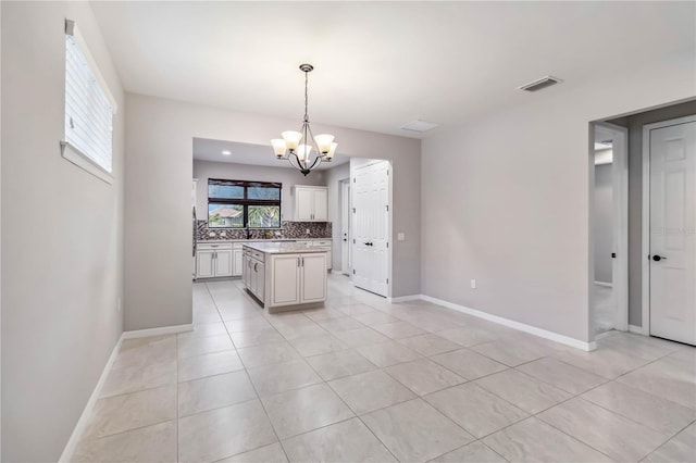 kitchen featuring an inviting chandelier, hanging light fixtures, a kitchen island, light tile patterned flooring, and decorative backsplash