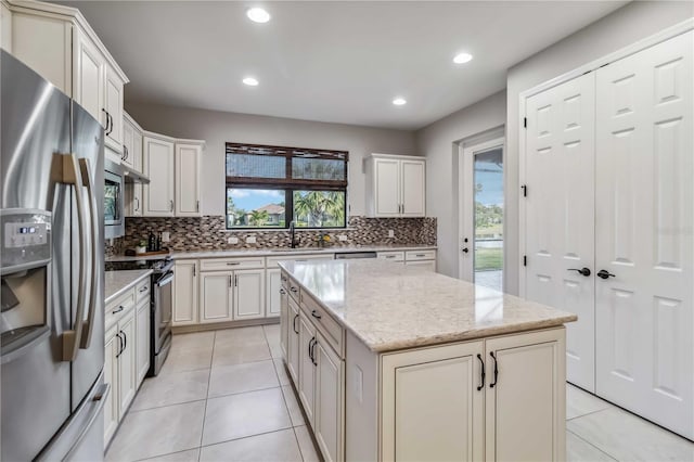 kitchen featuring sink, a center island, appliances with stainless steel finishes, light stone countertops, and decorative backsplash