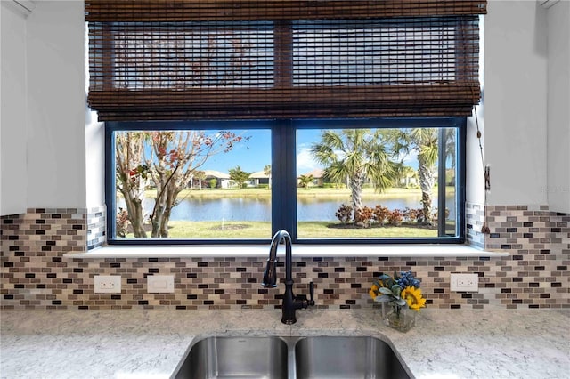 interior details featuring tasteful backsplash, a water view, sink, and light stone counters