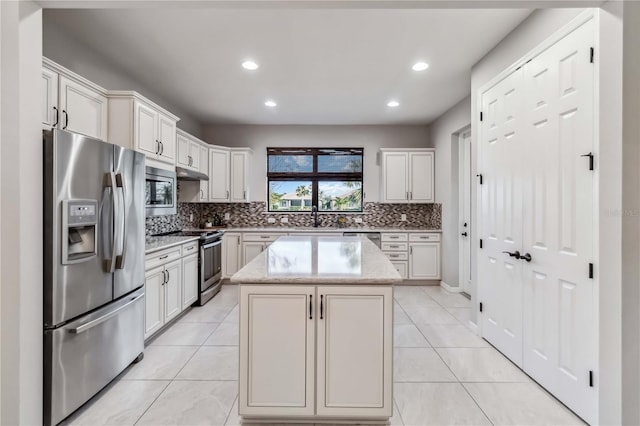 kitchen featuring stainless steel appliances, a center island, white cabinets, and light stone counters