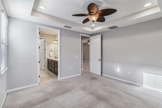 unfurnished bedroom with a raised ceiling, ceiling fan, light carpet, and ensuite bath