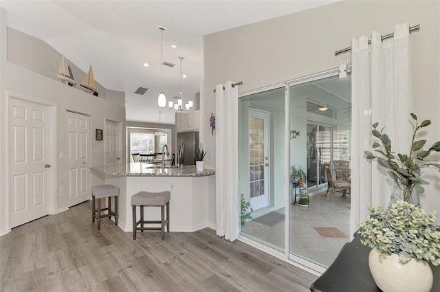 kitchen with pendant lighting, white cabinetry, light stone countertops, stainless steel fridge with ice dispenser, and vaulted ceiling