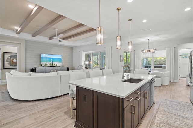 kitchen featuring sink, a kitchen bar, light stone counters, a center island with sink, and light wood-type flooring