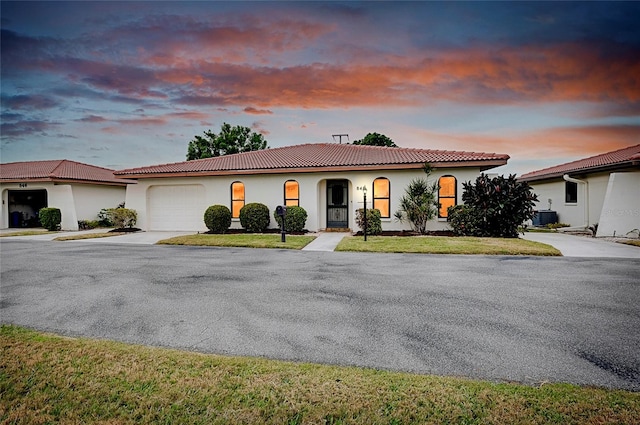 mediterranean / spanish-style house featuring a lawn, a garage, and central AC