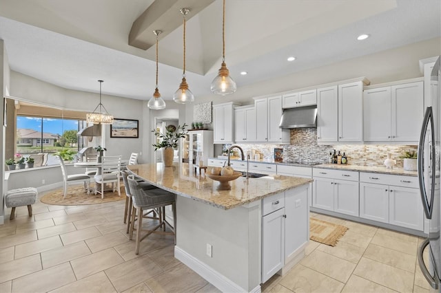 kitchen with sink, decorative light fixtures, an island with sink, light stone countertops, and white cabinets