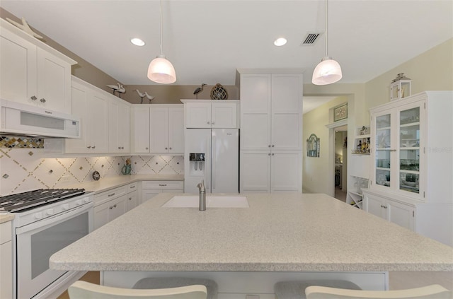 kitchen with white appliances, white cabinets, decorative light fixtures, sink, and a breakfast bar