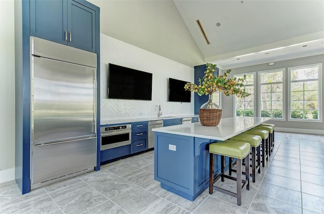 kitchen with a kitchen island, stainless steel appliances, blue cabinetry, sink, and a breakfast bar area