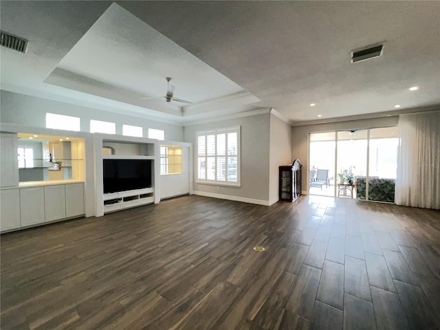 unfurnished living room featuring ceiling fan, dark wood-type flooring, a tray ceiling, and crown molding