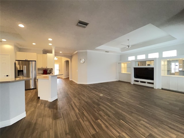 kitchen featuring stainless steel refrigerator with ice dispenser, ceiling fan, dark wood-type flooring, white cabinetry, and a tray ceiling