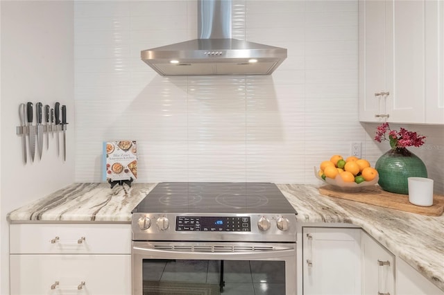 kitchen featuring stainless steel electric range oven, light stone countertops, white cabinets, and wall chimney exhaust hood