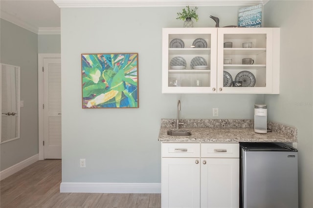 bar featuring sink, stainless steel refrigerator, ornamental molding, light stone countertops, and white cabinets