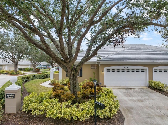 ranch-style home with a garage, driveway, a tile roof, and stucco siding