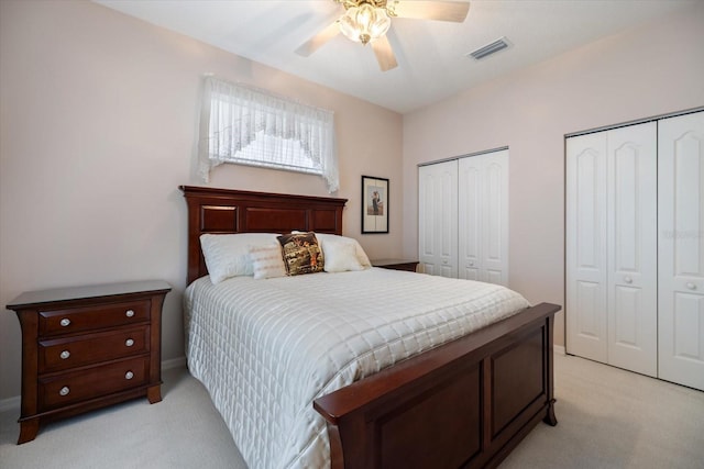 bedroom featuring multiple closets, light colored carpet, visible vents, and a ceiling fan