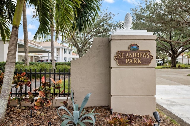 community sign featuring concrete driveway and fence