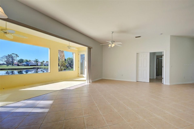 empty room with ceiling fan, a water view, and light tile patterned floors