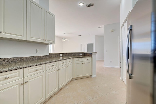 kitchen featuring dark stone countertops, stainless steel refrigerator, kitchen peninsula, and light tile patterned floors