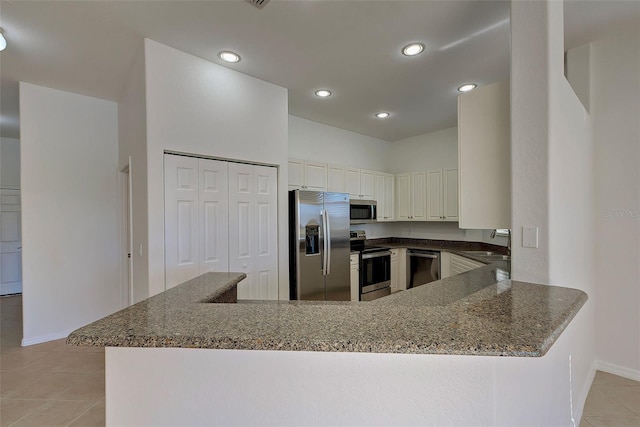 kitchen with dark stone counters, white cabinets, kitchen peninsula, and stainless steel appliances