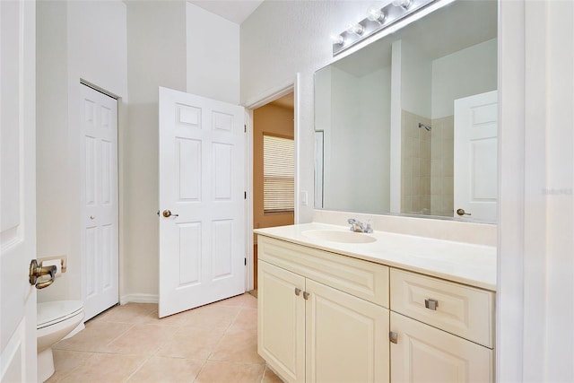 bathroom featuring vanity, toilet, a tile shower, and tile patterned flooring