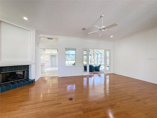 unfurnished living room featuring a tile fireplace, ceiling fan, ornamental molding, light hardwood / wood-style floors, and a textured ceiling