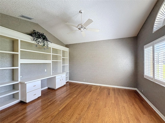 unfurnished office featuring built in desk, vaulted ceiling, a textured ceiling, hardwood / wood-style flooring, and ceiling fan