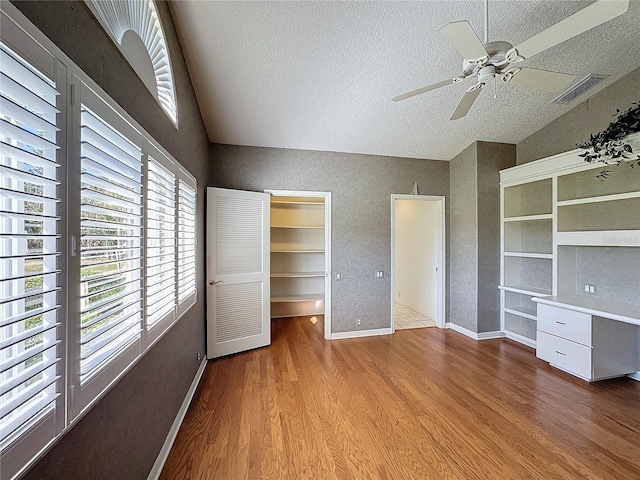 unfurnished bedroom with vaulted ceiling, light wood-type flooring, a spacious closet, ceiling fan, and a textured ceiling