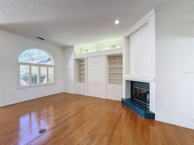 unfurnished living room featuring hardwood / wood-style floors, crown molding, a tile fireplace, and a textured ceiling