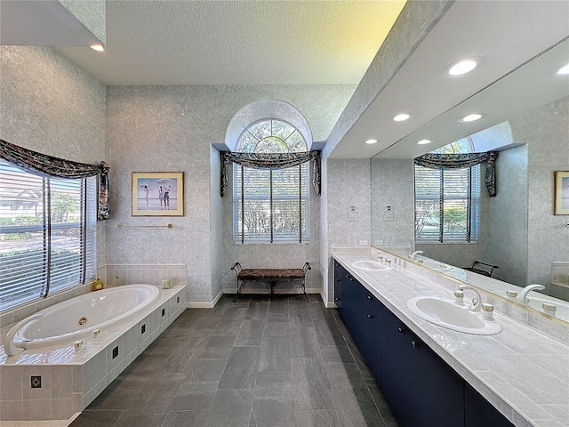 bathroom with vanity, a healthy amount of sunlight, tiled bath, and a textured ceiling