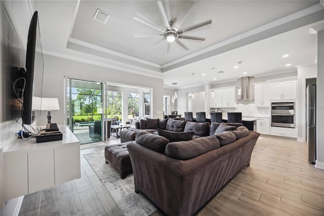 living room with a raised ceiling, crown molding, and ceiling fan