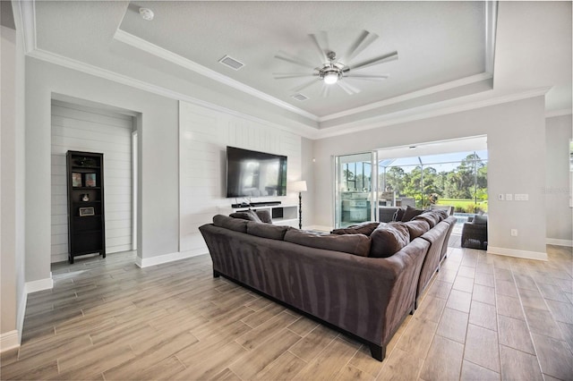 living room featuring a raised ceiling, ornamental molding, and ceiling fan