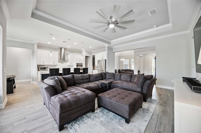 living room with ornamental molding, a tray ceiling, and ceiling fan with notable chandelier