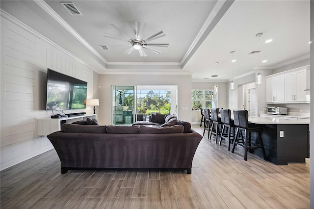 living room featuring a raised ceiling, ornamental molding, ceiling fan, and a textured ceiling