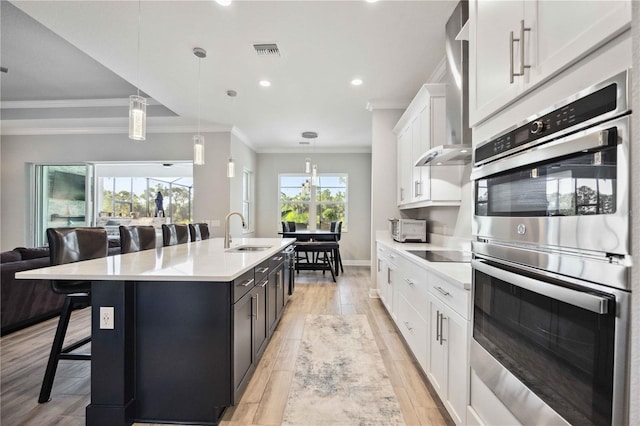 kitchen featuring a kitchen bar, sink, white cabinetry, decorative light fixtures, and a kitchen island with sink