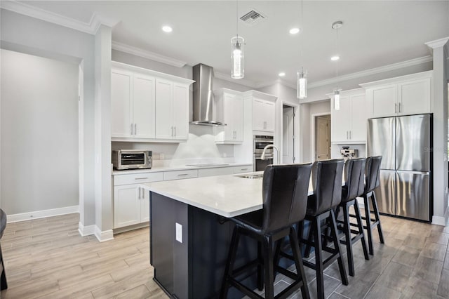 kitchen with white cabinetry, wall chimney range hood, stainless steel appliances, and hanging light fixtures