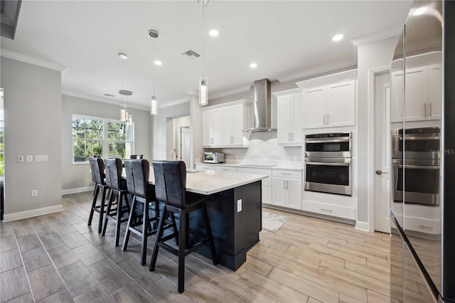 kitchen with a kitchen island with sink, wall chimney range hood, white cabinets, and stainless steel double oven