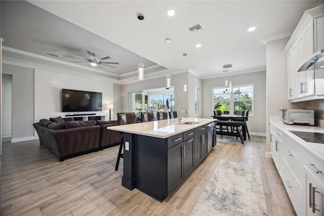 kitchen featuring sink, hanging light fixtures, ornamental molding, a kitchen island with sink, and white cabinets