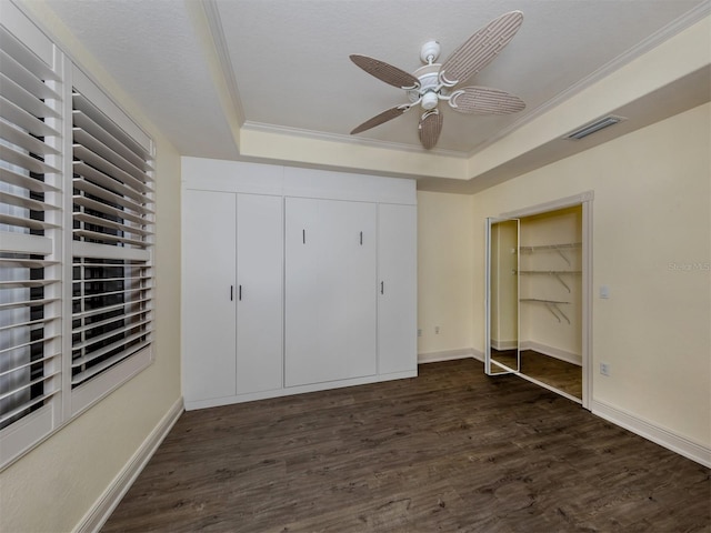 unfurnished bedroom featuring crown molding, dark wood-type flooring, ceiling fan, a tray ceiling, and a closet