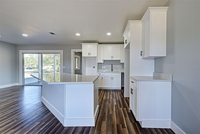 kitchen featuring dark wood-type flooring, sink, a kitchen island, light stone countertops, and white cabinets