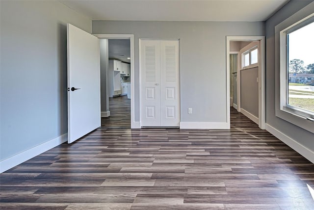 unfurnished bedroom with a closet, multiple windows, wood finished floors, and baseboards