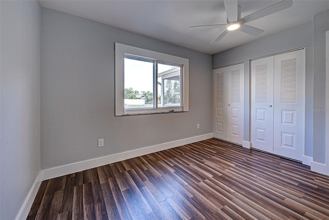 unfurnished bedroom featuring two closets, ceiling fan, baseboards, and dark wood-type flooring