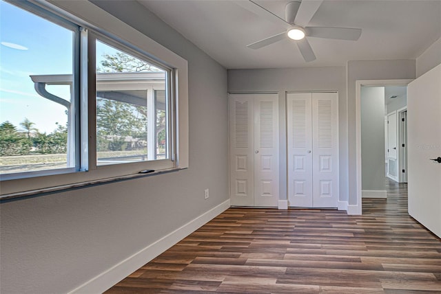 unfurnished bedroom featuring a ceiling fan, baseboards, dark wood finished floors, and multiple closets