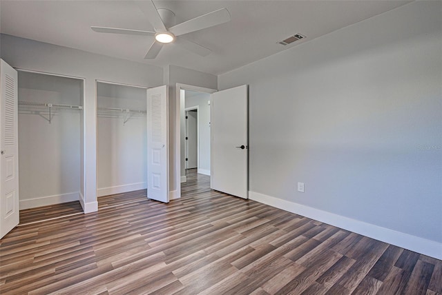 unfurnished bedroom featuring ceiling fan, hardwood / wood-style floors, and two closets