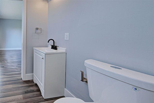 half bathroom with baseboards, vanity, toilet, and wood finished floors