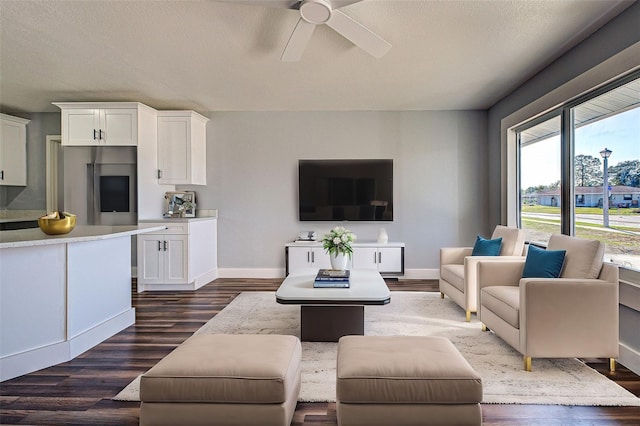 living area with a textured ceiling, dark wood-type flooring, a ceiling fan, and baseboards