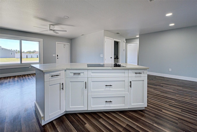 kitchen with dark wood-style flooring, black electric stovetop, light countertops, white cabinetry, and baseboards