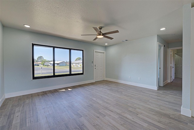 empty room with light wood finished floors, baseboards, visible vents, and a textured ceiling